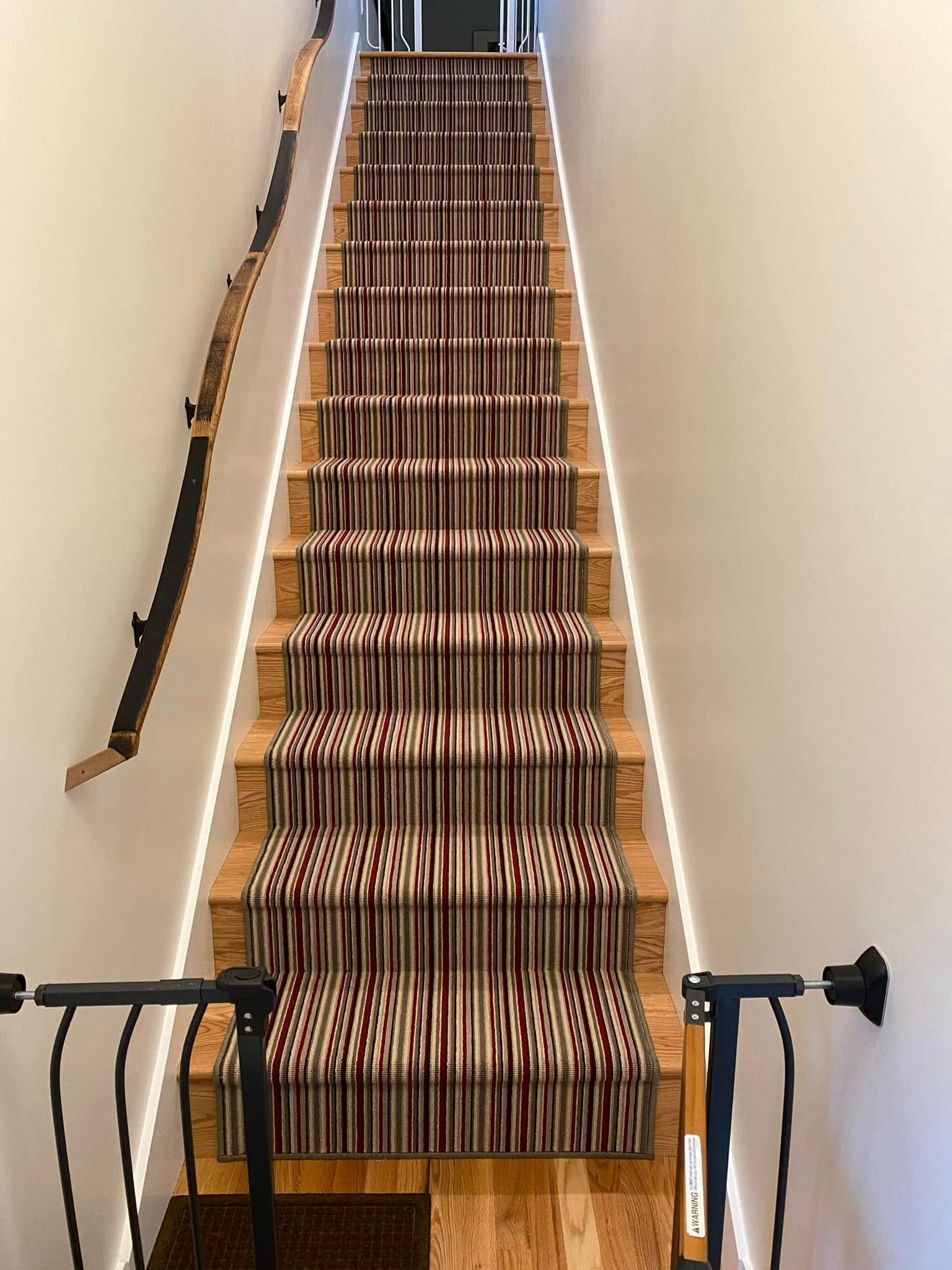 Staircase with striped runner, wood treads, black handrail on the left, and white walls.