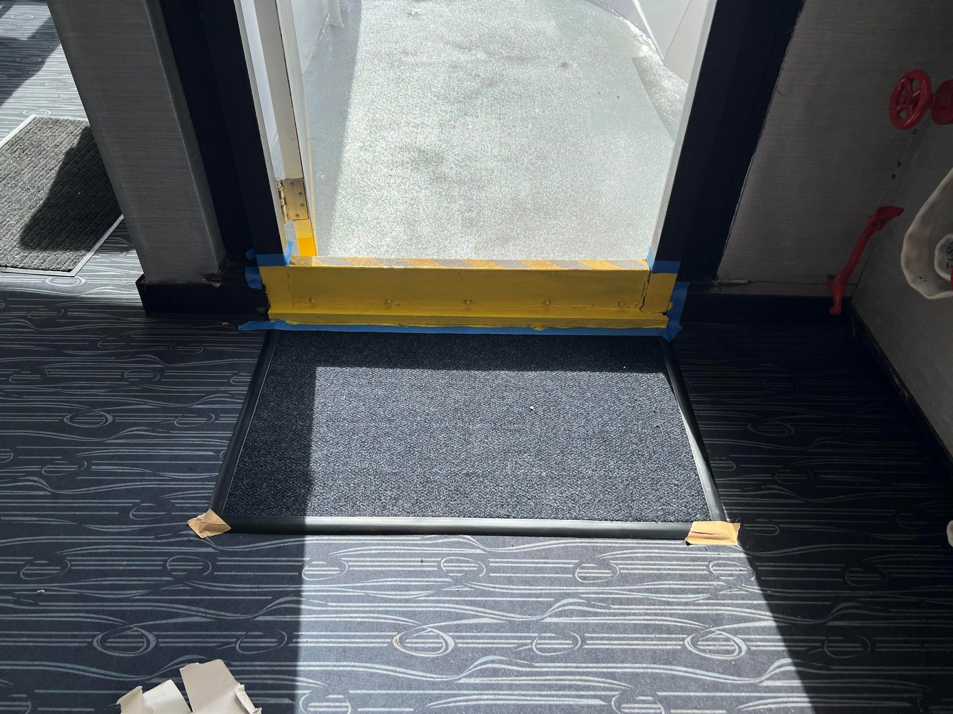 Doorway with yellow threshold, blue tape, welcome mat, and patterned flooring.