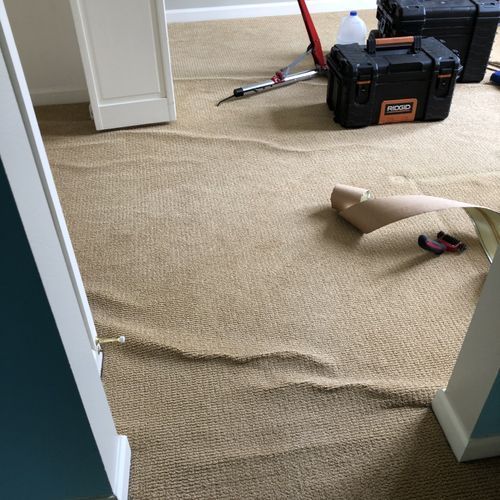 Tan carpet with visible ripples, tools, and open doorway, suggesting installation.