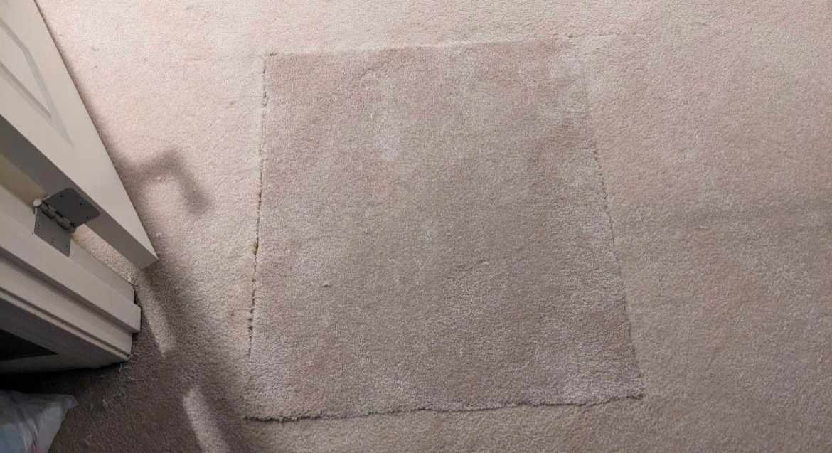 Square-shaped area on beige carpet shows lighter color, possibly from a rug, near a white door frame.