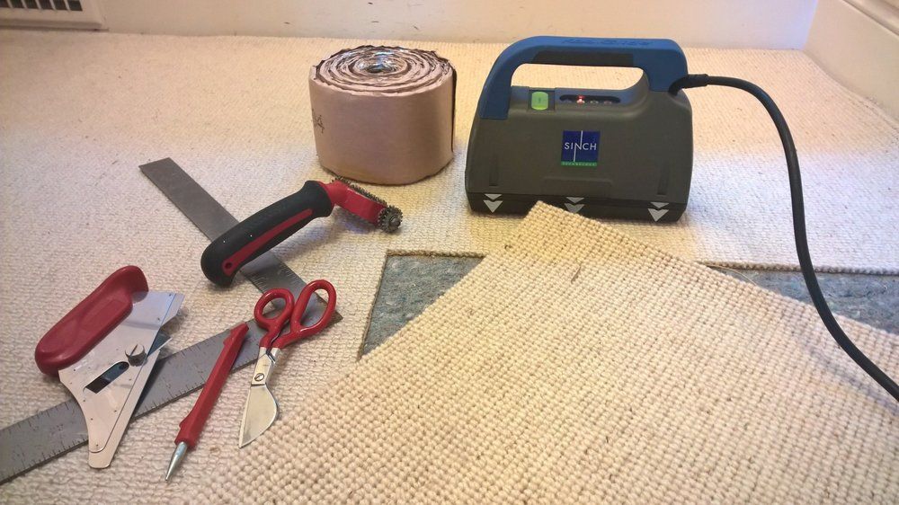 Carpet installation tools and materials: cutter, scissors, seam roller, power stretcher, and tape.