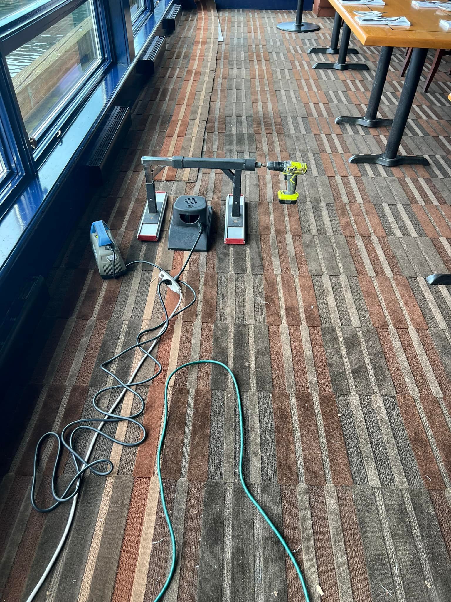 A robotic arm prototype with tools on a striped carpet next to a window and tables.