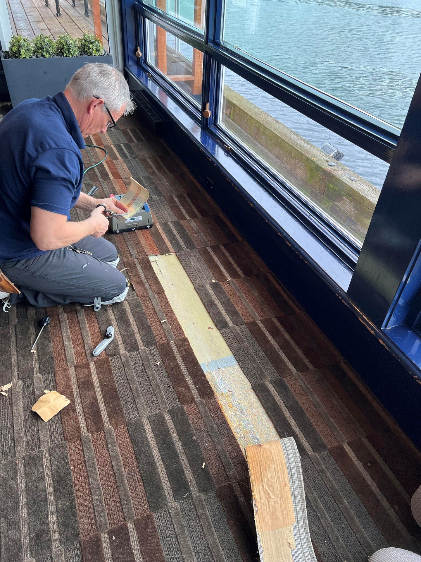 Man installing flooring by large window overlooking water.