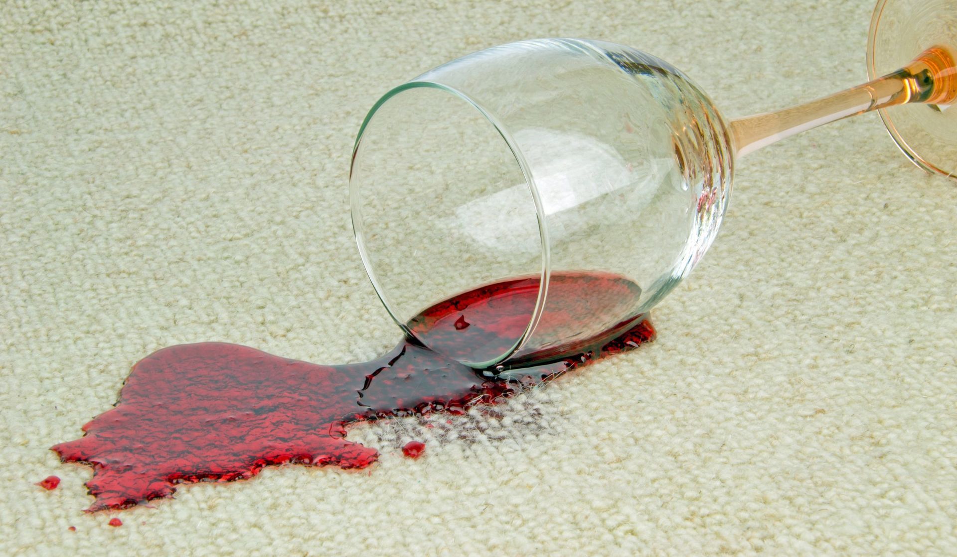 Spilled red wine on a beige carpet, with an overturned wine glass.