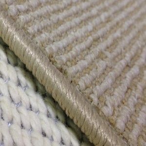 Close-up of a beige carpet with a stitched edge next to a white knitted fabric.
