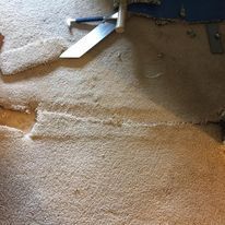 Carpet being repaired, with a visible seam and tools: knife and hammer.
