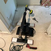 Carpet installation tools in a doorway, including a power drill, knee kicker, and scissors.