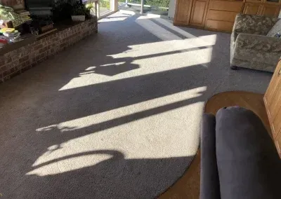 Sunlight and shadows across beige carpet in a room with a fireplace, cabinets, and a chair.