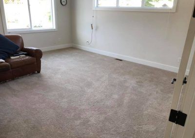 A room with light-colored carpet, a brown leather sofa, and two windows.