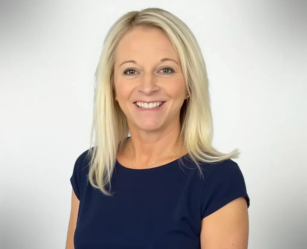 Blonde woman smiling, wearing a navy blue top, against a white background.