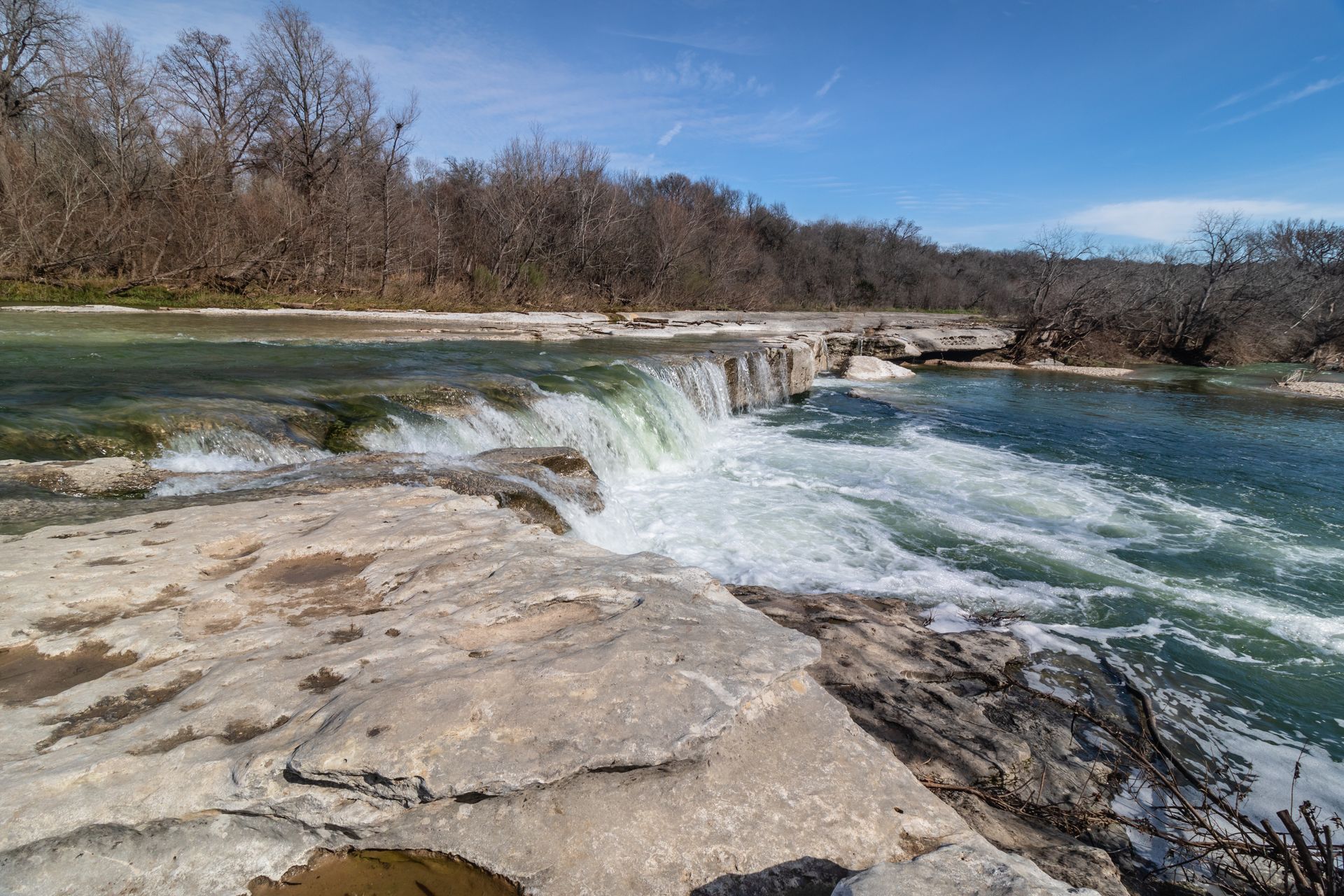 A waterfall is surrounded by rocks and trees in the middle of a river.