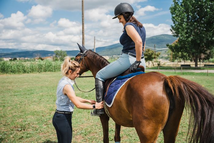 A woman is helping another woman ride a horse in a field.