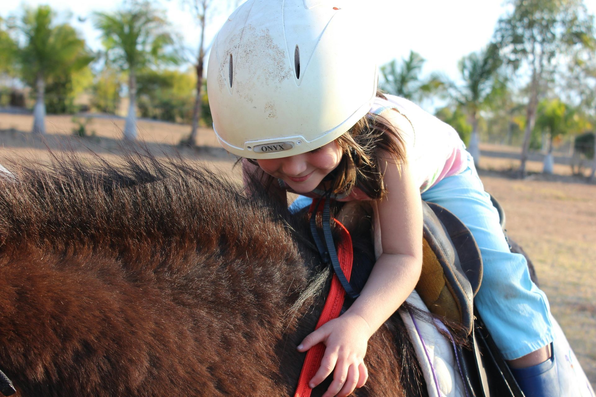 A little girl wearing a white helmet is petting a brown horse