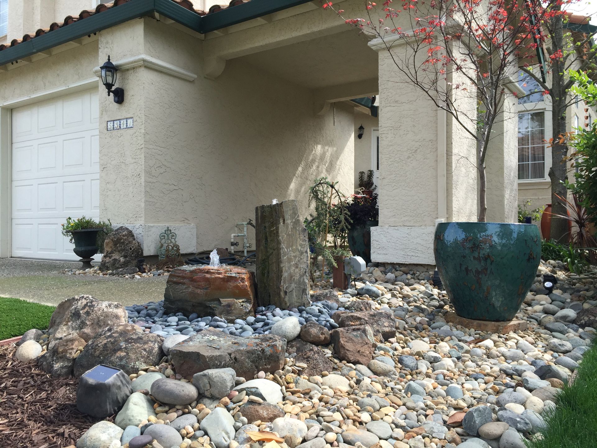 A house with a fountain and rocks in front of it.