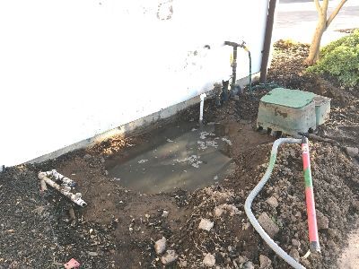 A hose is sitting in the dirt next to a white wall.