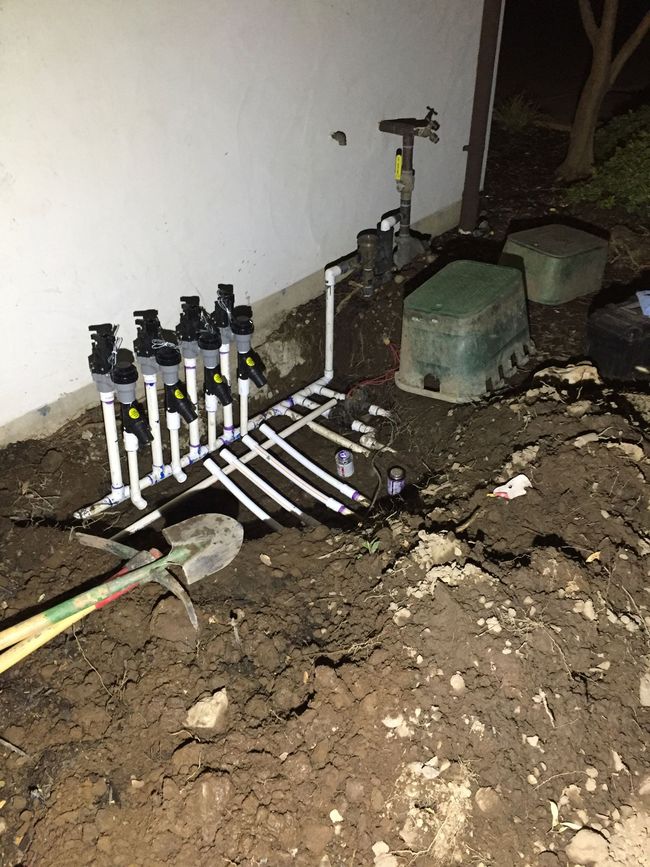 A sprinkler system is being installed in the dirt in front of a house.