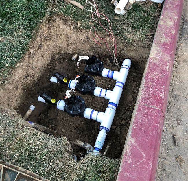 A bunch of pipes are sitting in the dirt next to a red curb.