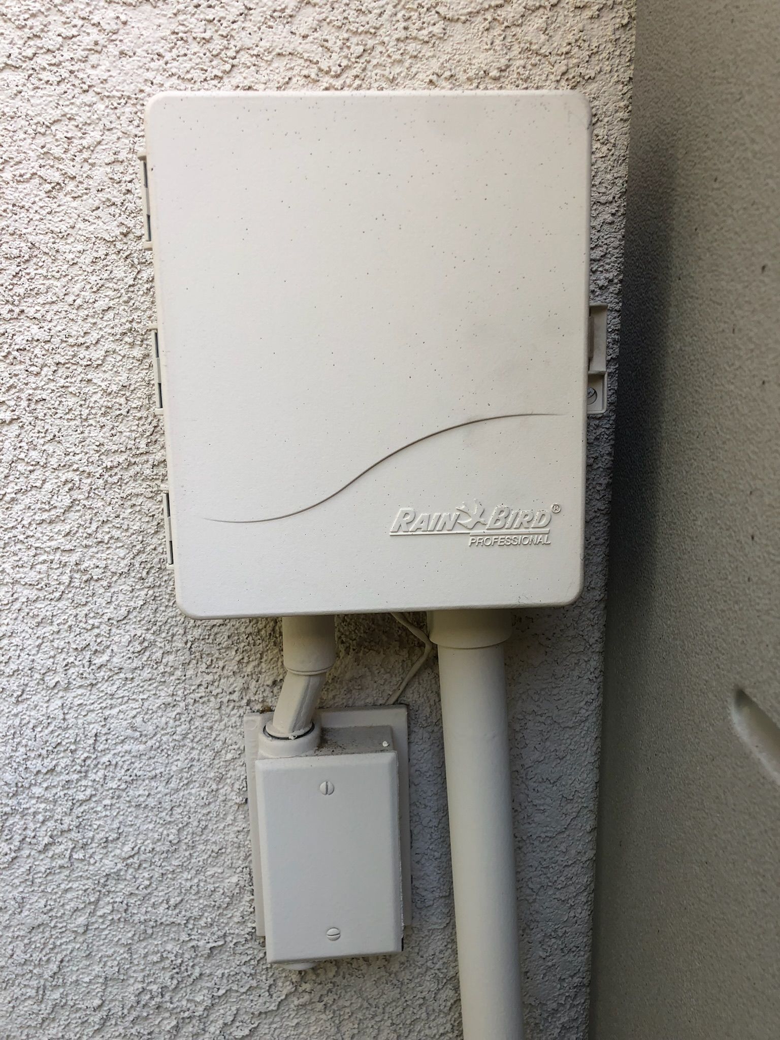 A white box is hanging on a wall next to a pipe.