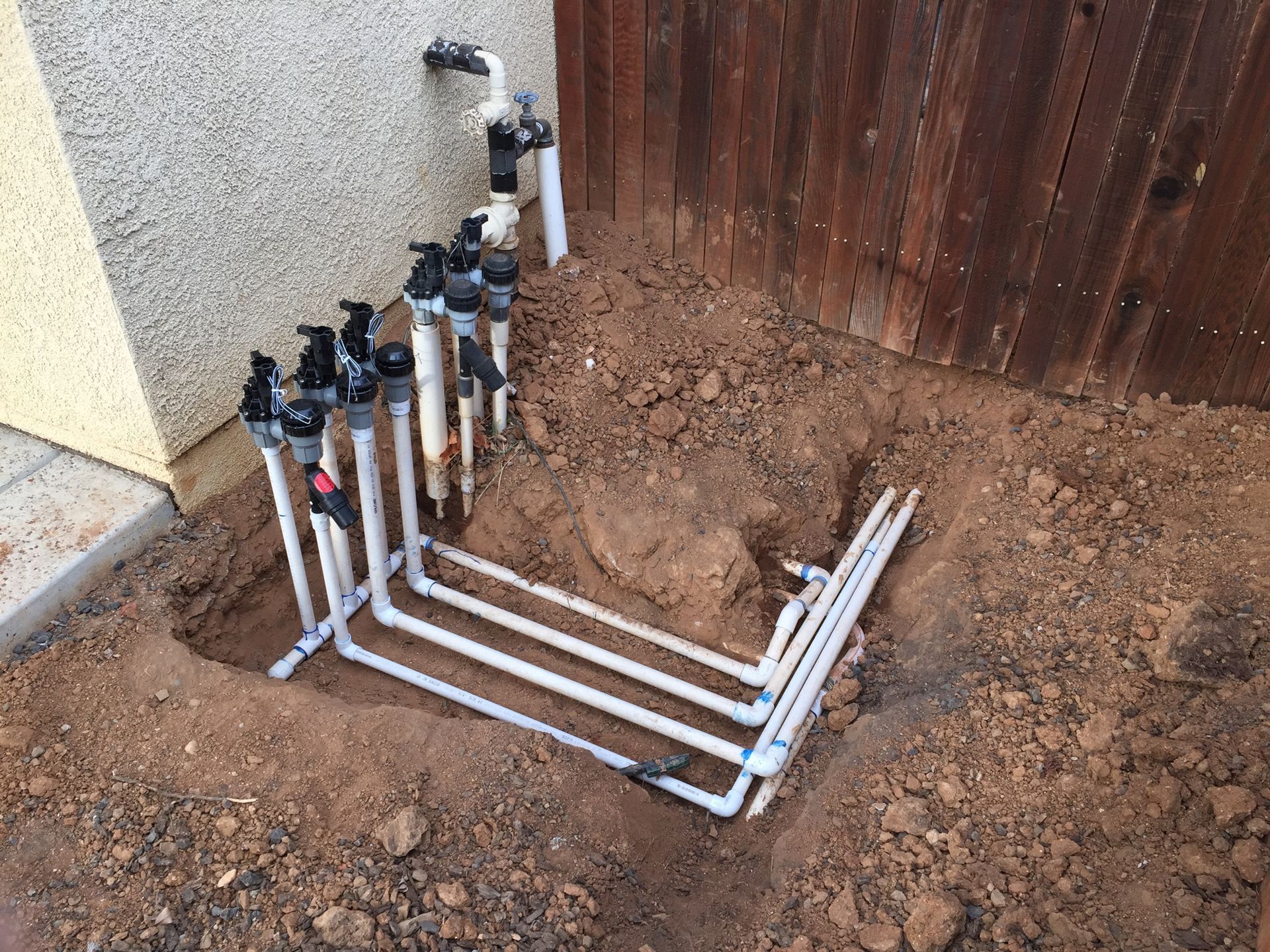 A bunch of pipes are sitting in the dirt next to a wooden fence.