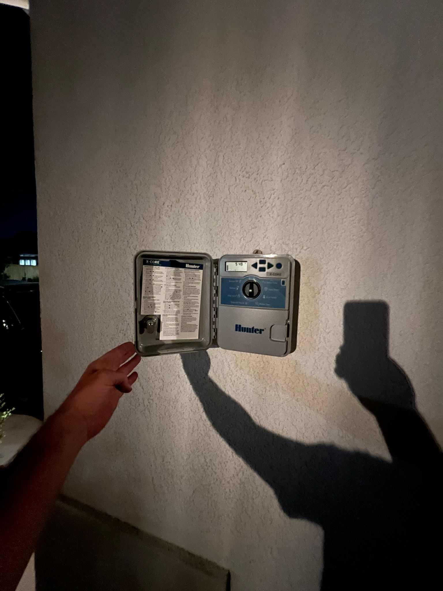 A person is holding a sprinkler controller on a wall.