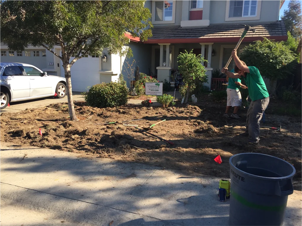 A man is digging in the dirt in front of a house.