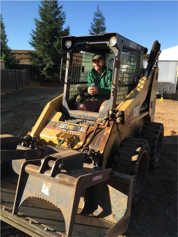 A man in a green jacket is driving a cat bulldozer