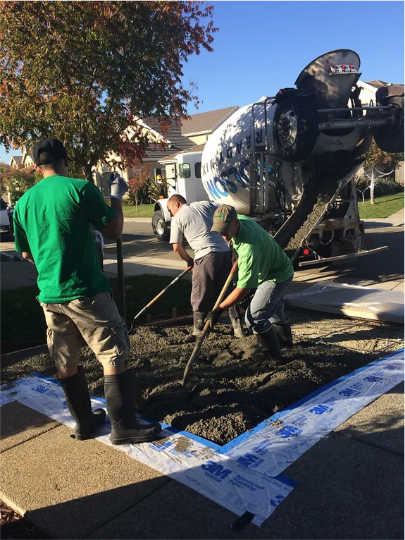 A group of men are working on a sidewalk in front of a cement truck.