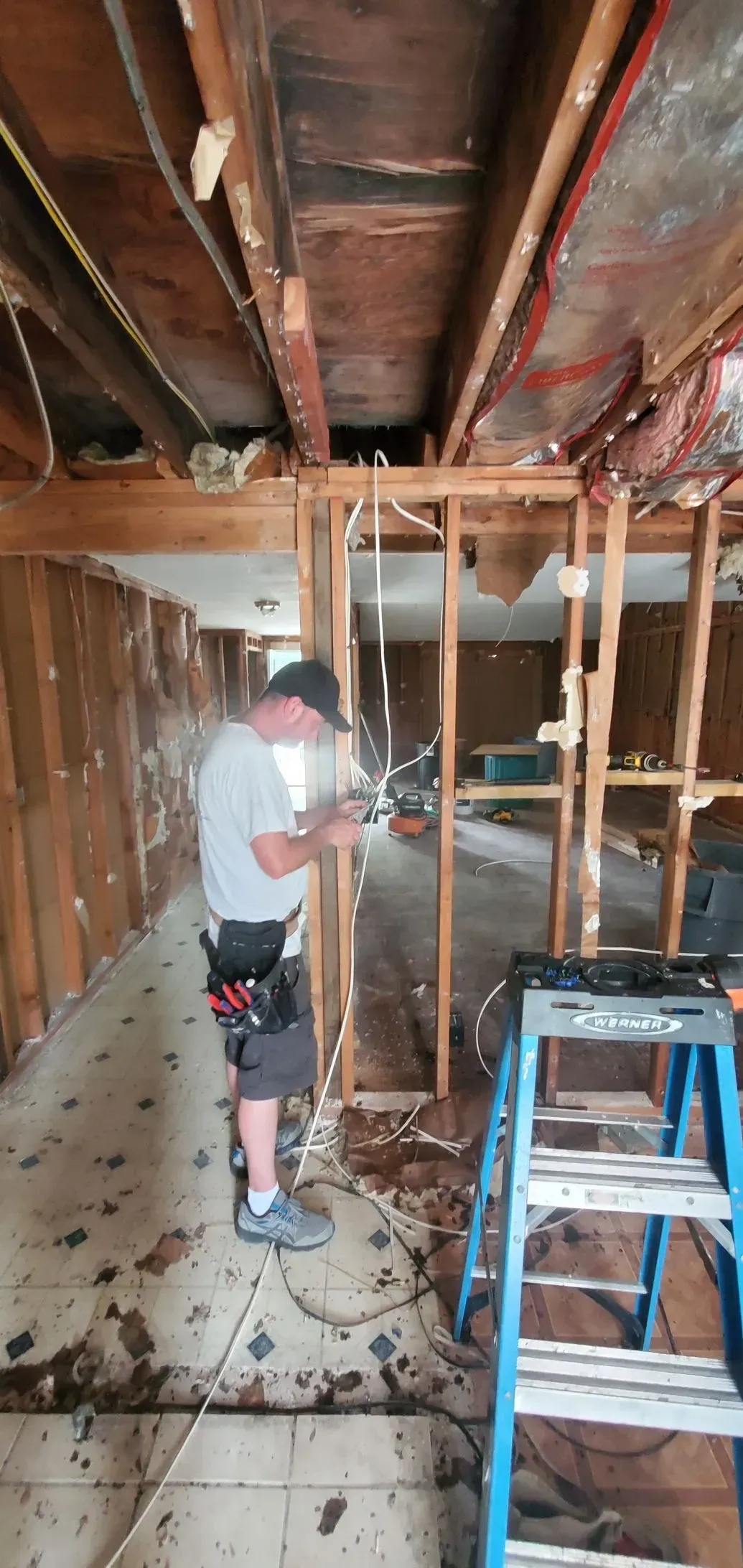 A man is working on a wall in a room with a ladder.