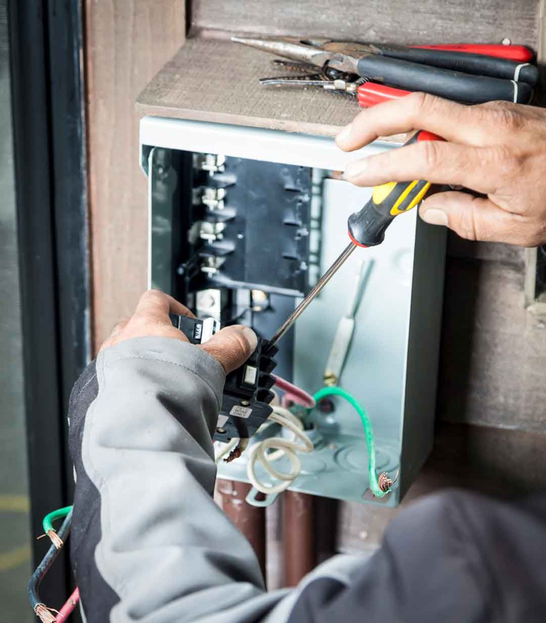 A person is working on an electrical box with a screwdriver and pliers.