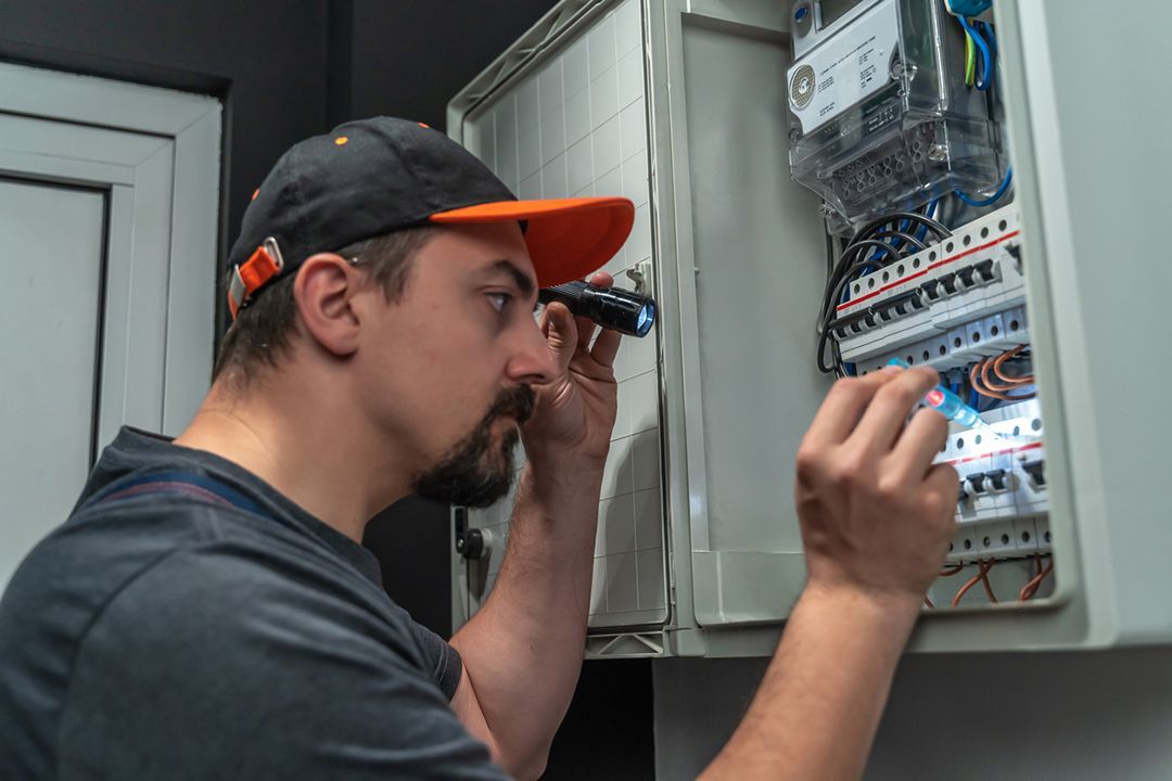 A man is working on an electrical box with a flashlight.