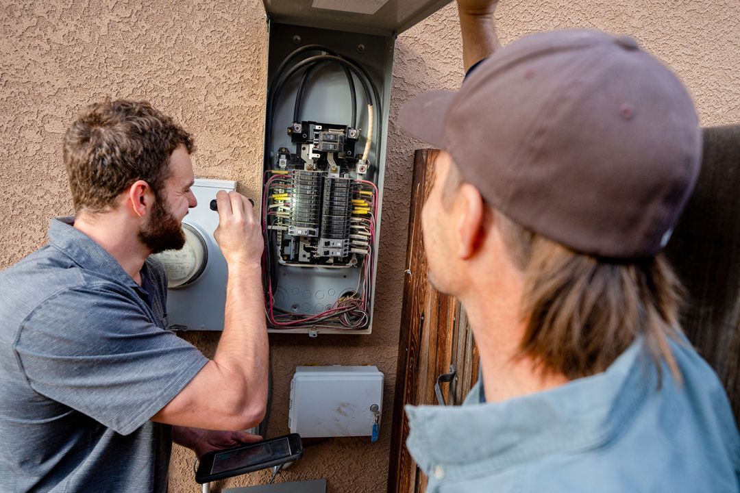 Two men are working on an electrical box on the side of a building.