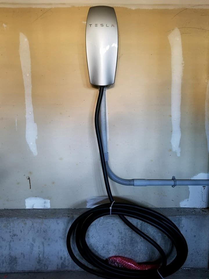 A tesla charging station is attached to a wall in a garage.