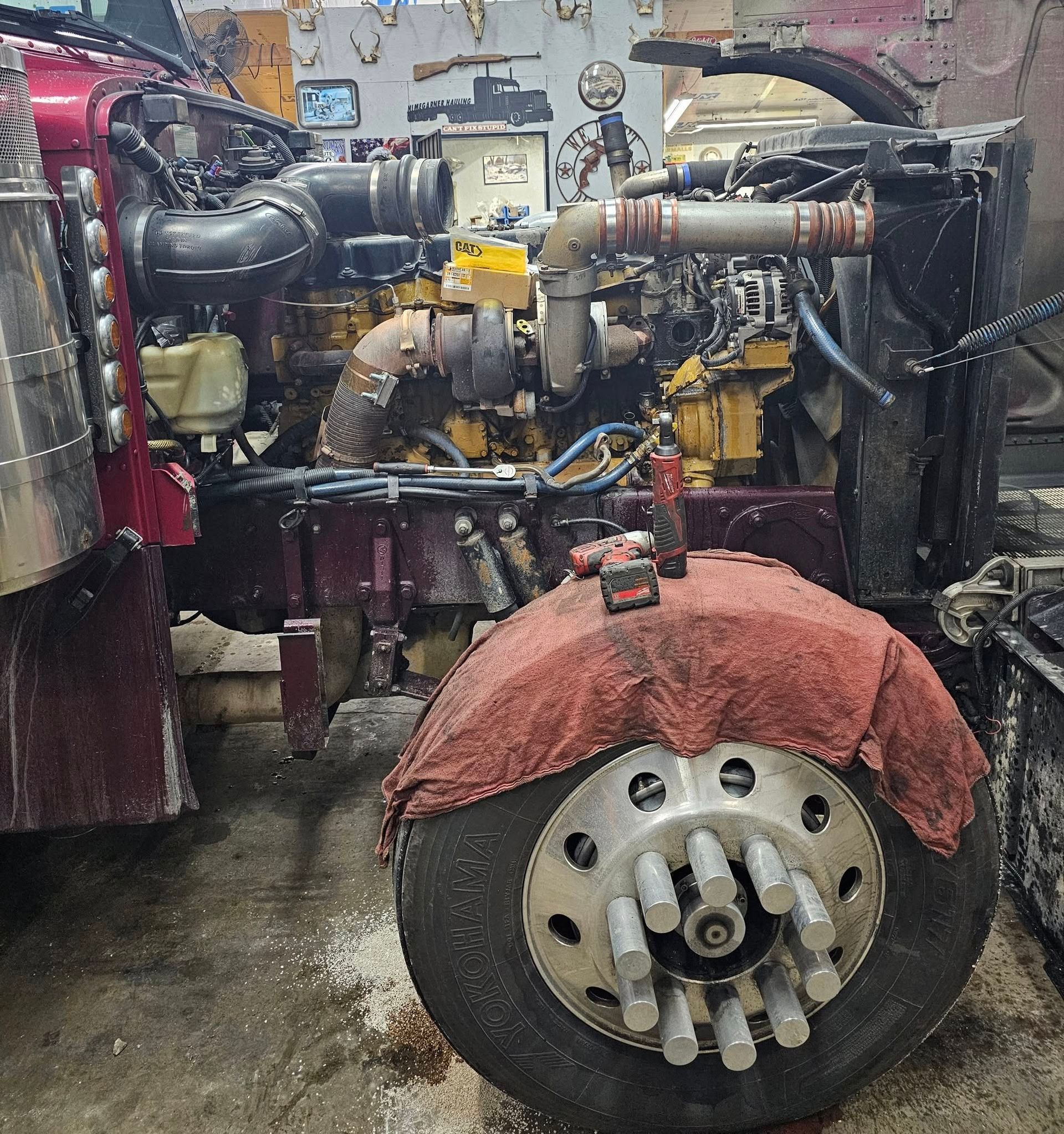 Semi-truck engine being worked on in a repair shop; wheel covered with red cloth.