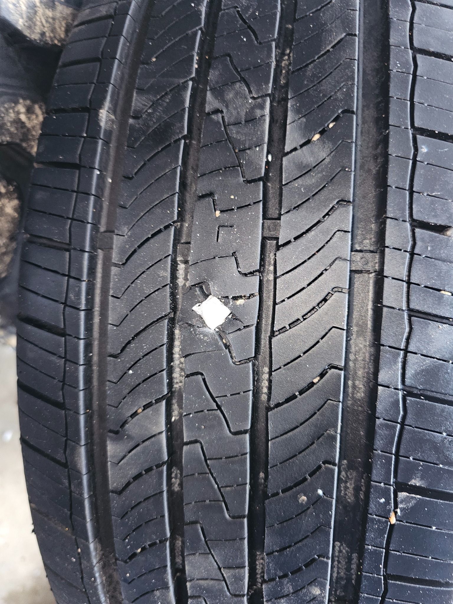 Close-up of a black tire tread with a small, white rectangular object embedded in its surface.
