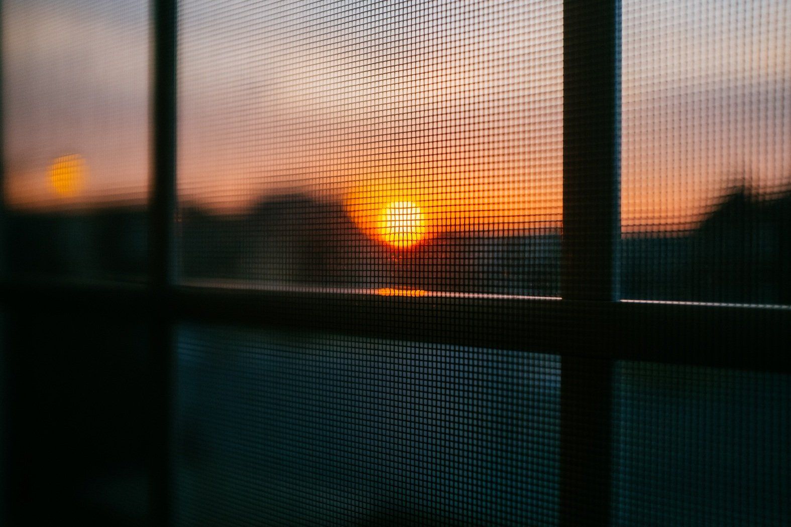 Sunset view through a window screen, casting a warm glow on a cozy interior.