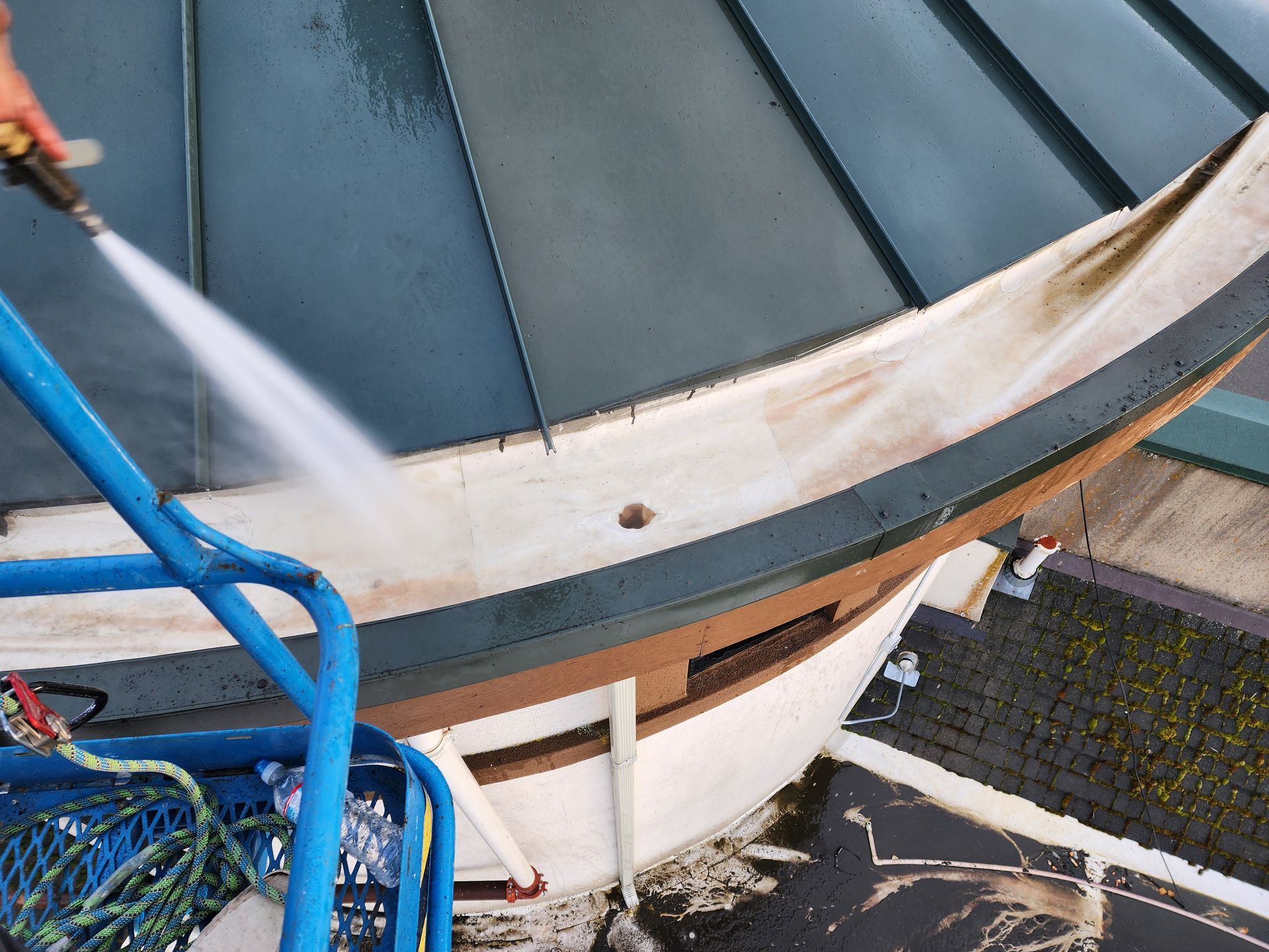 A person on a lift power washes the white and green trim of a domed roof.