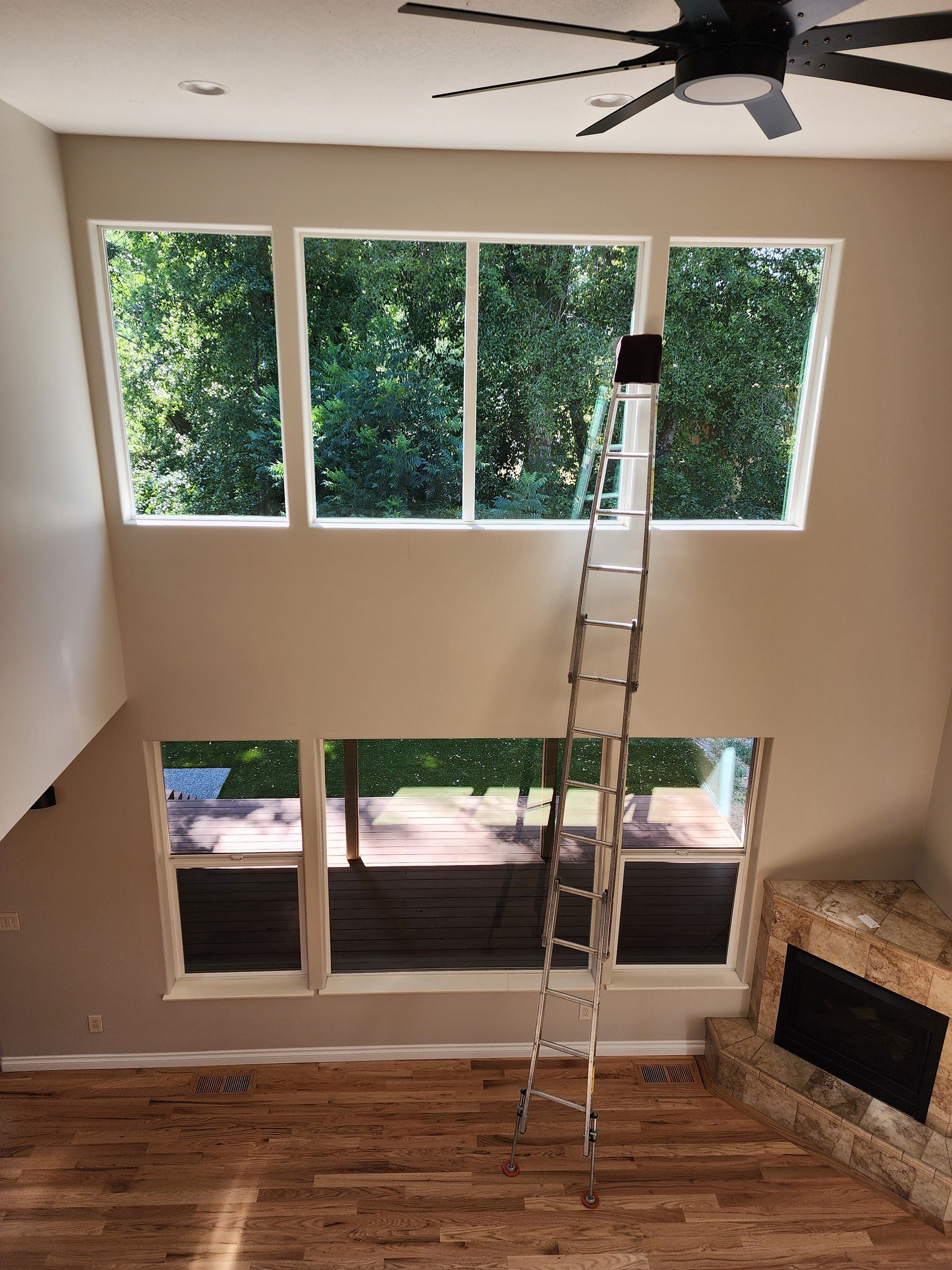 Tall windows with a ladder inside a room.  A person is up the ladder near the windows.
