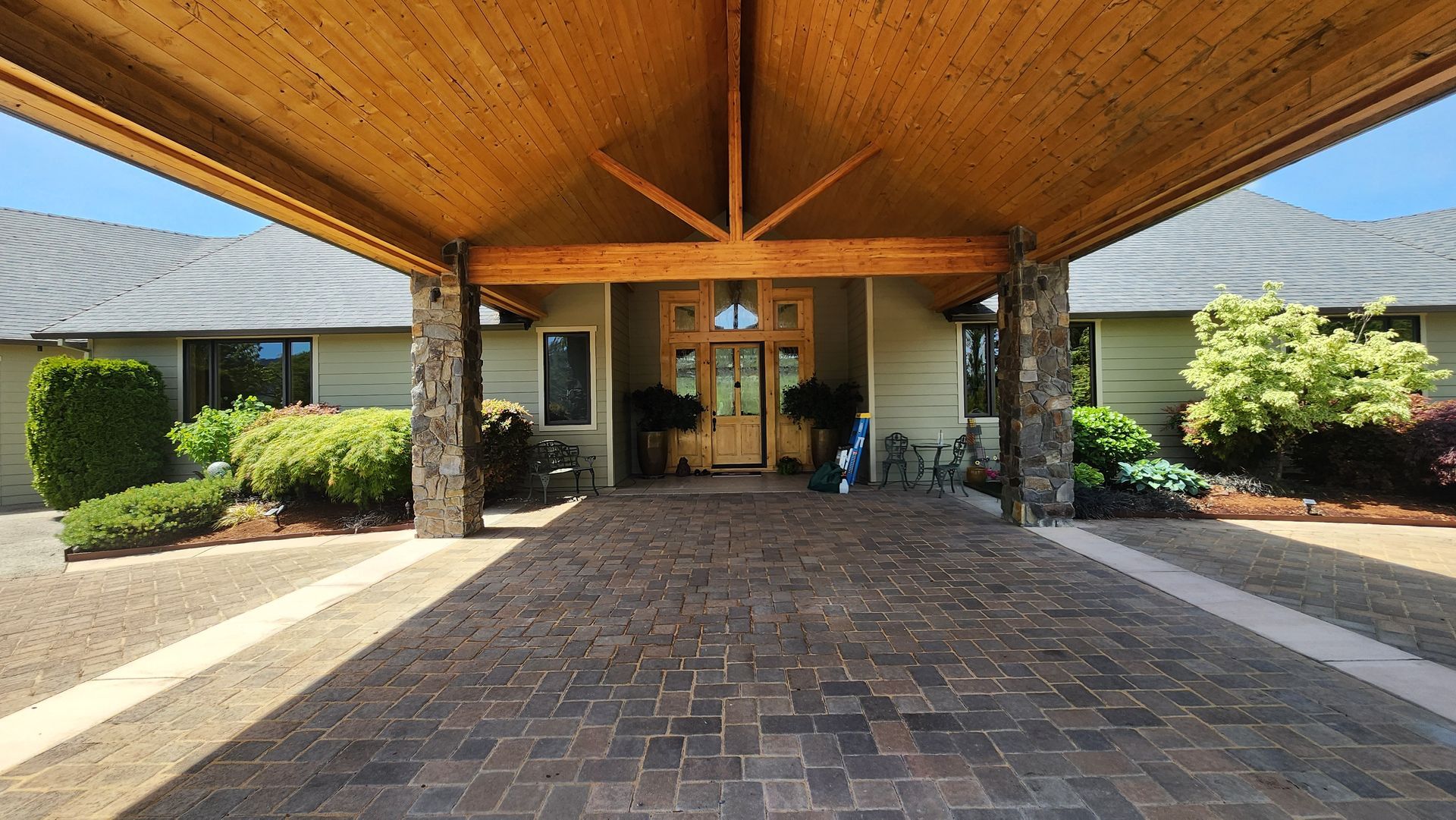 Carport entrance to a house with stone pillars, brick pavers, and wooden ceiling.