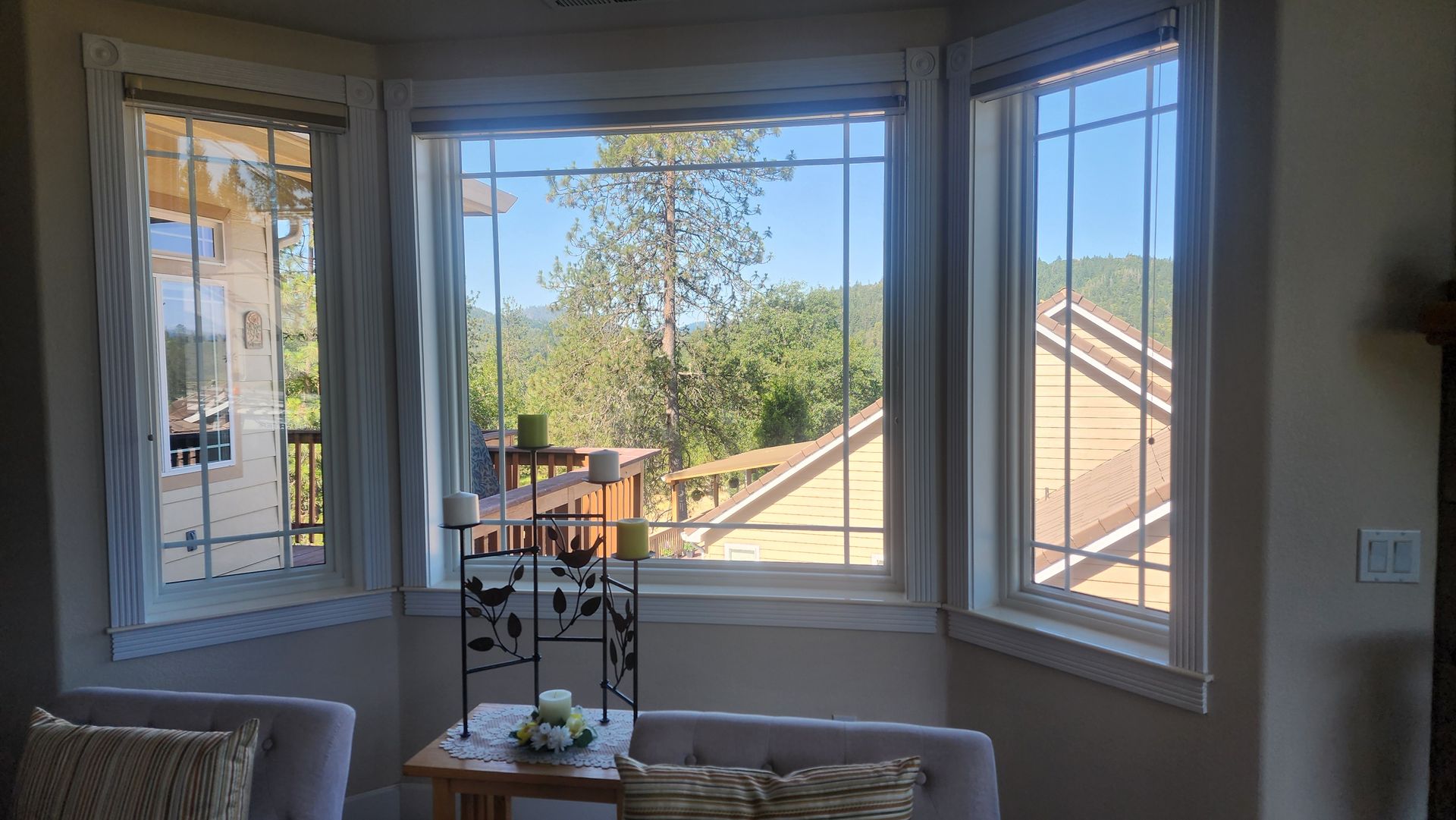 Bay window with scenic view of trees and house, interior with chairs and side table.