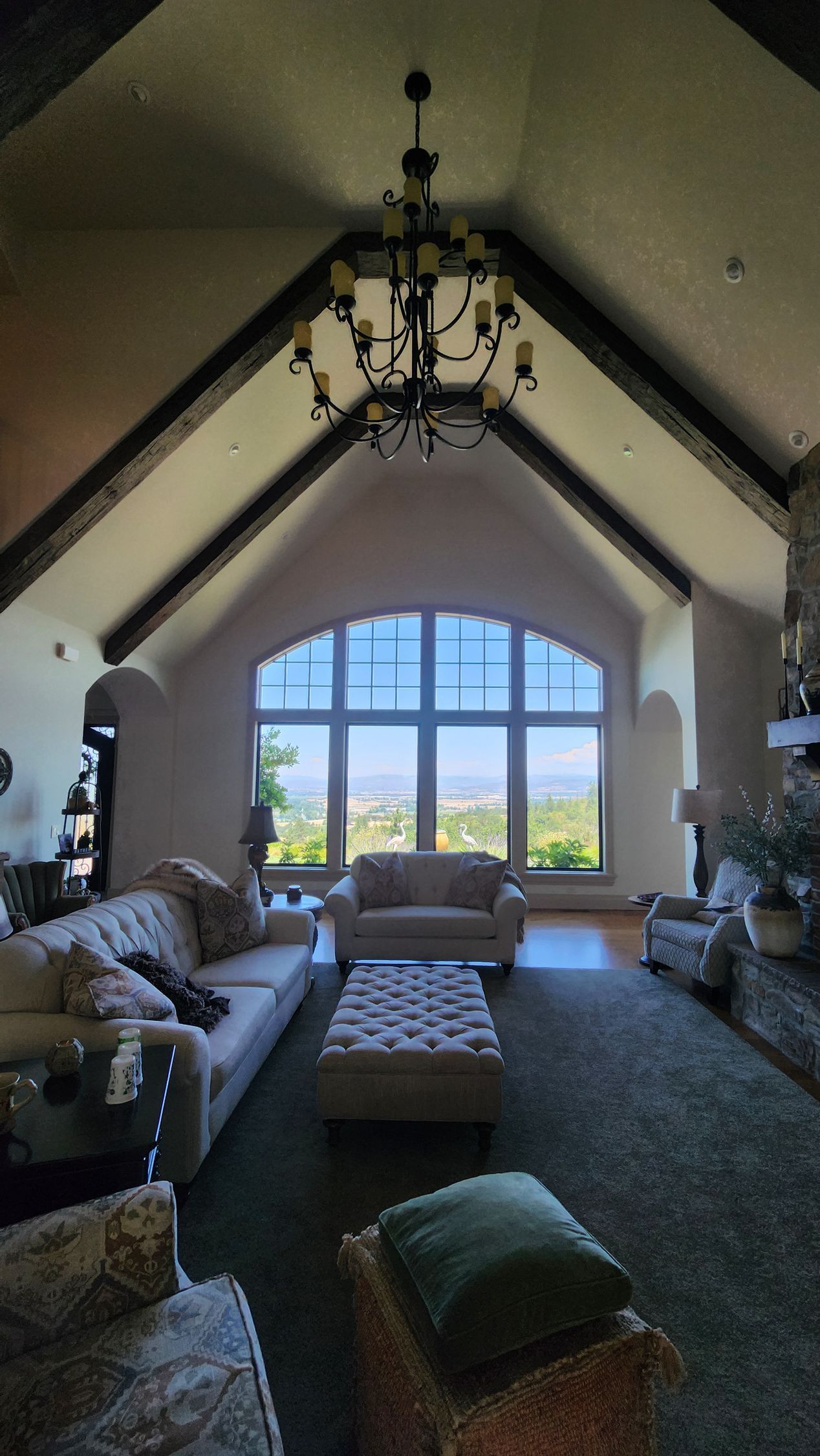 Living room with vaulted ceiling, large window, couches, and chandelier.