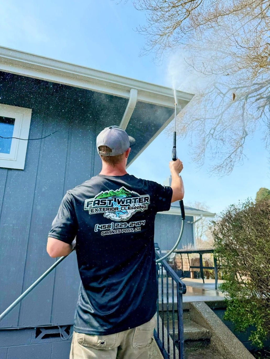 Man power washing a house gutter on a sunny day.