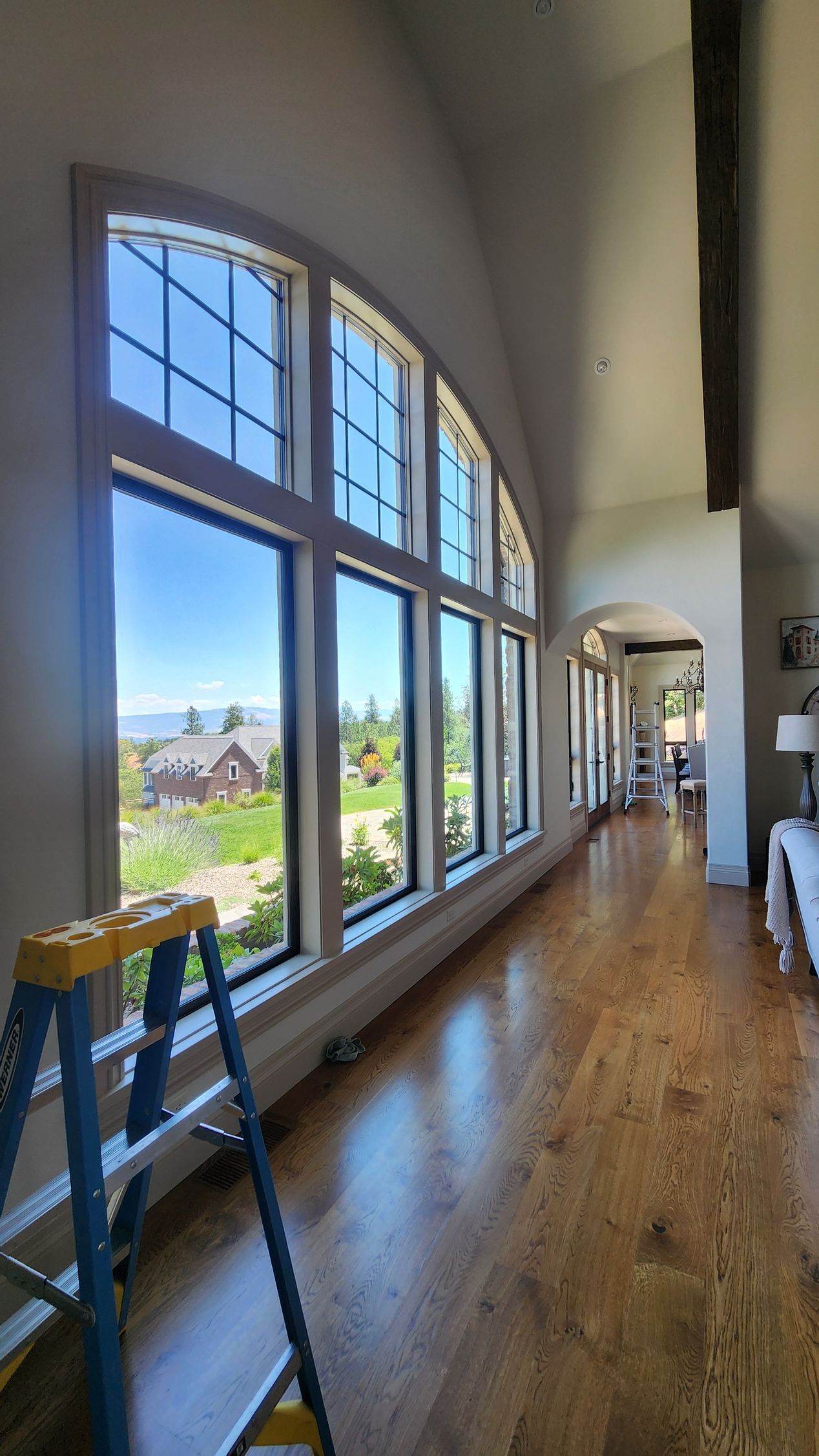 Long hallway with arched windows and blue sky view; a stepladder leans against the windows.