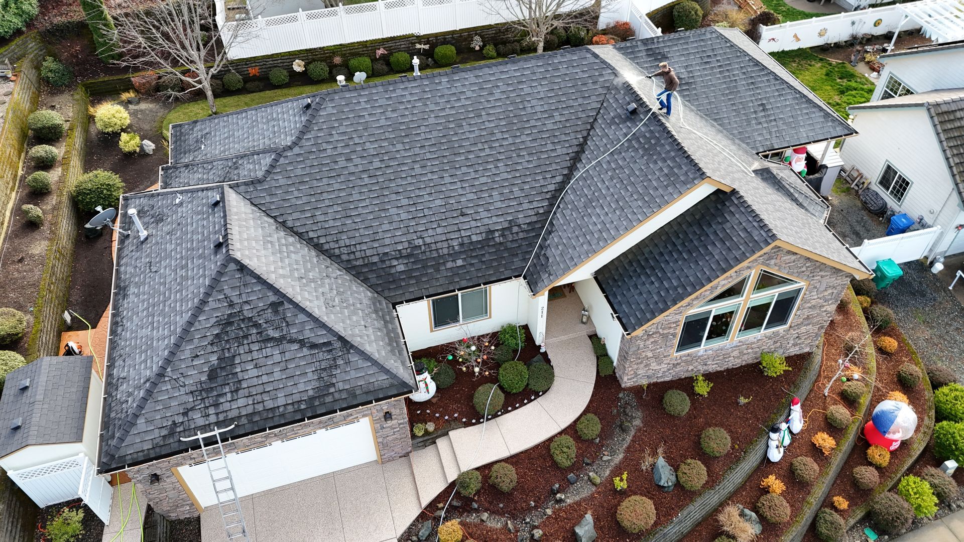 Aerial view of a house with a dark gray roof, landscaping, and a brick facade.