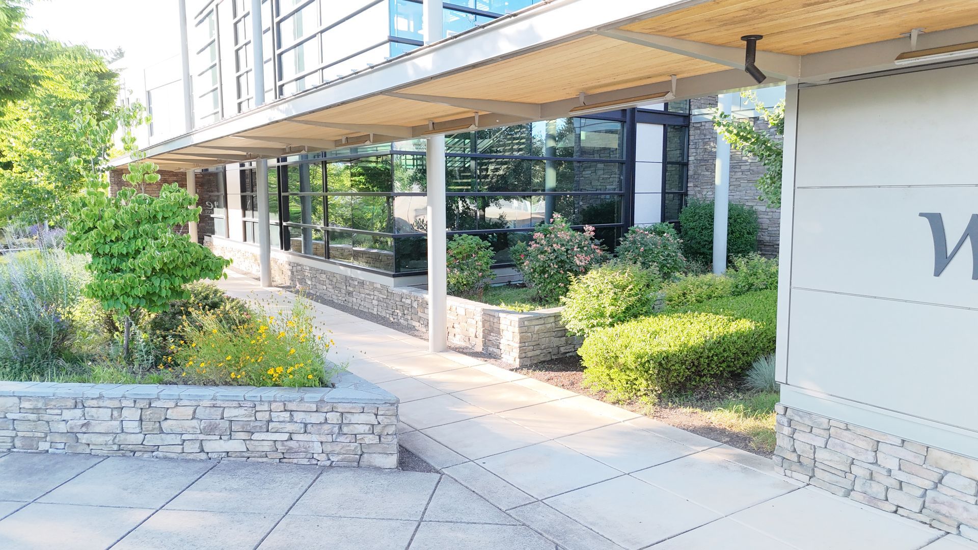 Modern building with a stone walkway and landscaped garden, sunny day.