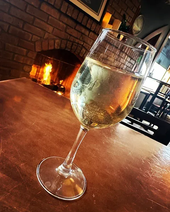 A glass of wine is sitting on a table in front of a fireplace.