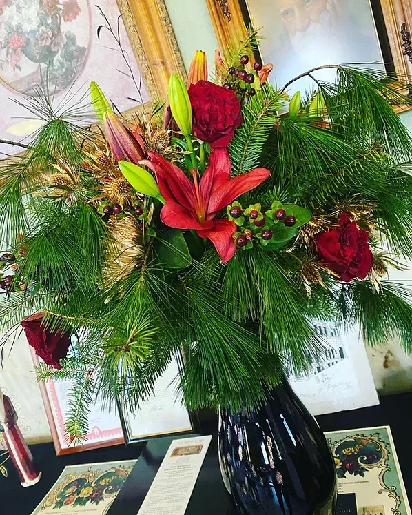 A vase filled with flowers and pine needles is sitting on a table.