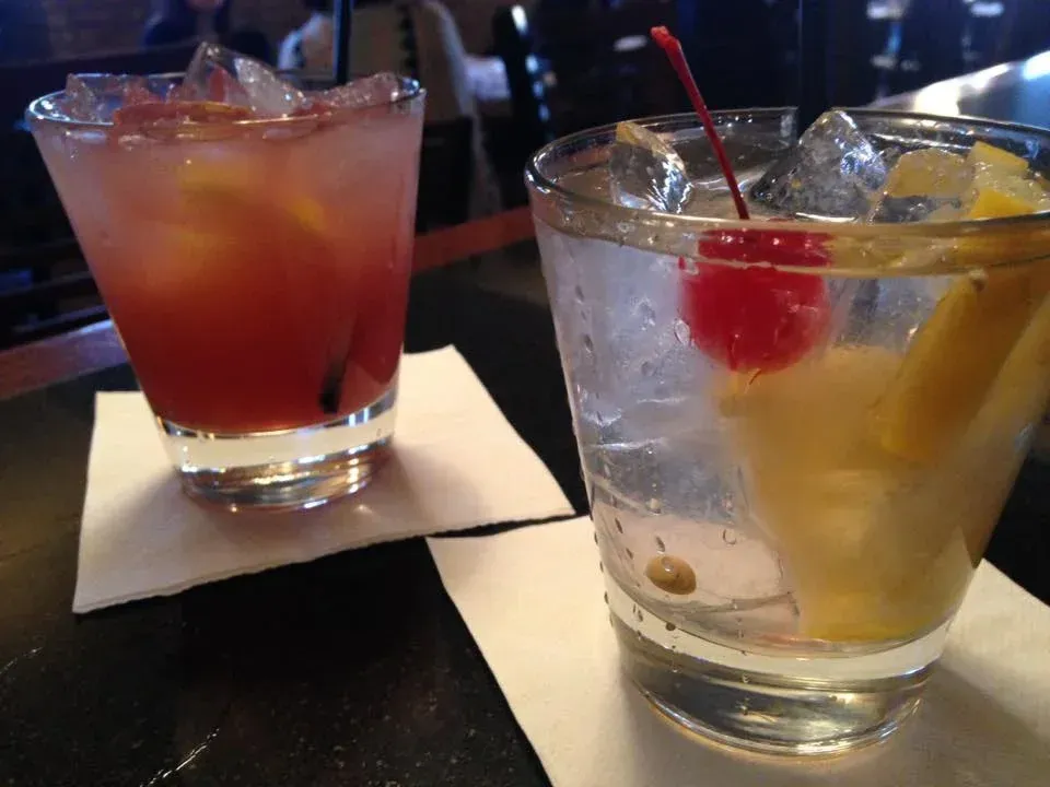 Two drinks with ice and a cherry on top are on a napkin on a table.