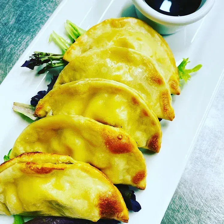A white plate topped with fried dumplings and sauce