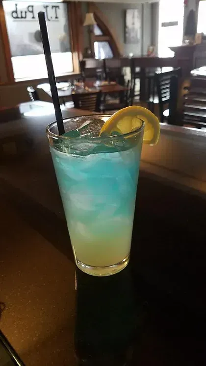 A blue and yellow drink with a straw and a lemon slice on a table.