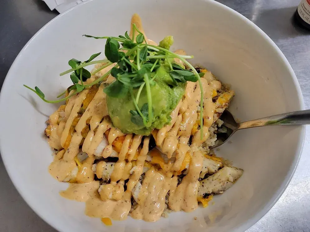 A bowl of food with guacamole on top and a fork in it.